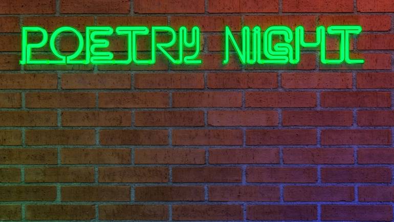 fluorescent poetry night sign on a brick wall