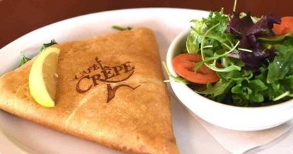 A plate that has a crepe and a salad on it