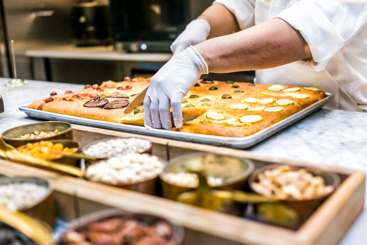 chef wearing gloves slices focaccia bread