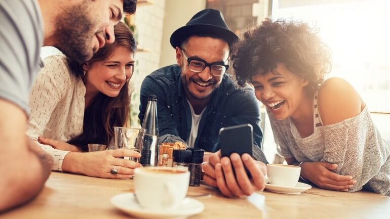 Group of friends looking at a smartphone screen in a cafe