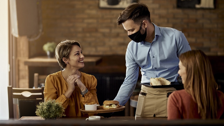 Waiter wearing a face mask serving food to customers in a pub