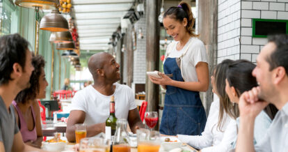 Happy waitress taking orders to a group of people eating together at a restaurant.