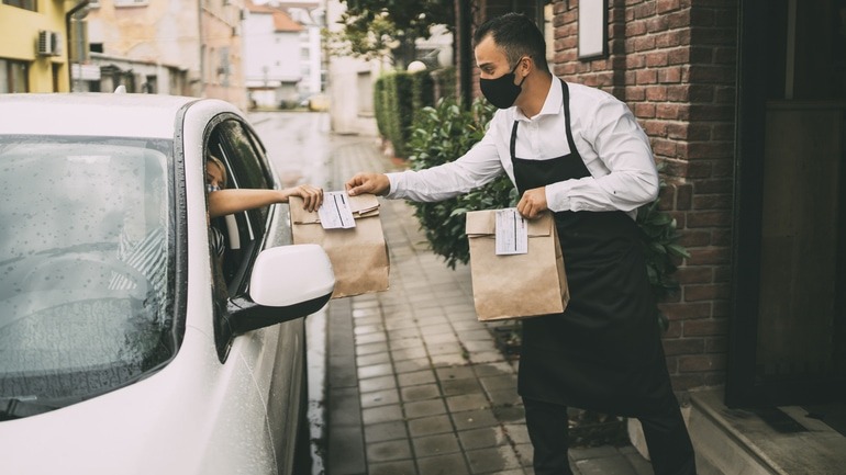 Male restaurant employee delivers packed food to a female driver outside a restaurant