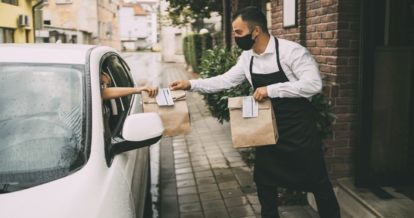 Restaurant employee handing food orders to a delivery driver