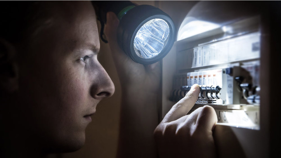 person inspecting fuse box with a flashlight
