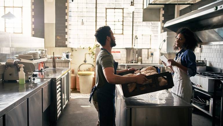server bringing tray of baked bread into restaurant kitchen