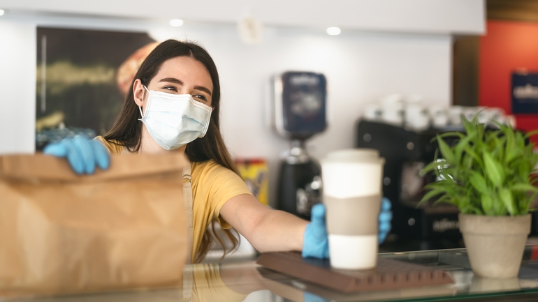 Young cafe worker wearing a face mask while giving a meal to customers