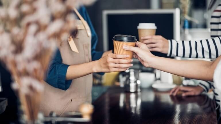 Barista serving a takeaway hot coffee cup to customer at counter bar in cafe restaurant
