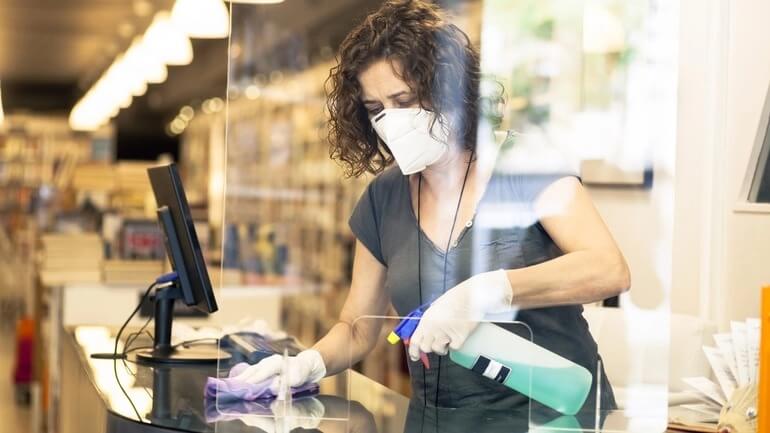 A woman cleaning a checkout counter while wearing a face mask.