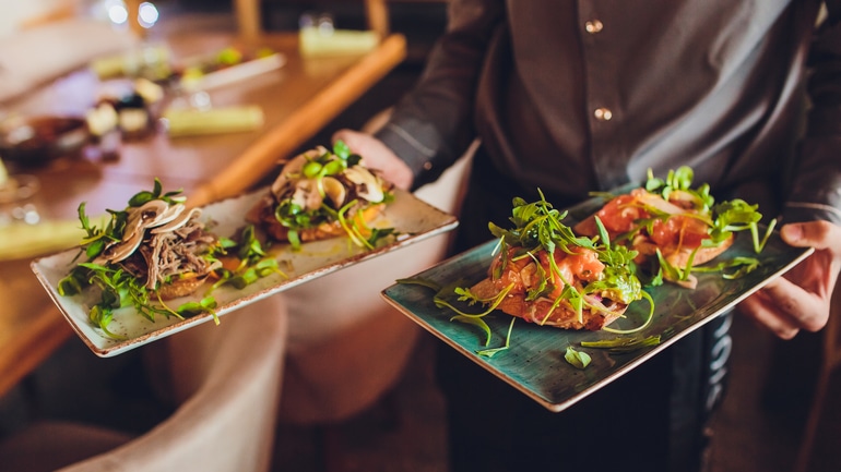 Two meat plate with salad leaves and summer salad in waiter's hand.