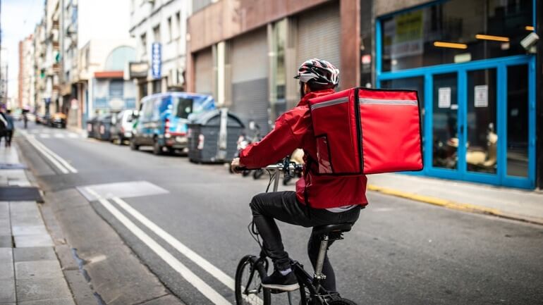 A man riding his bike down the street going to deliver food.