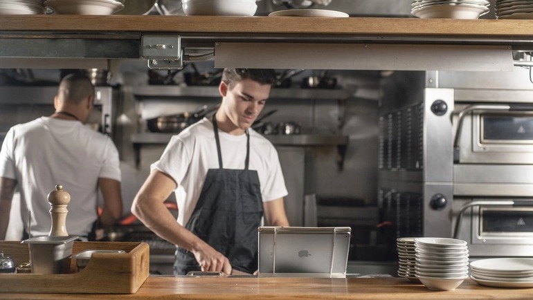 Line cook prepping food behind a restaurant counter in front of a restaurant KDS.