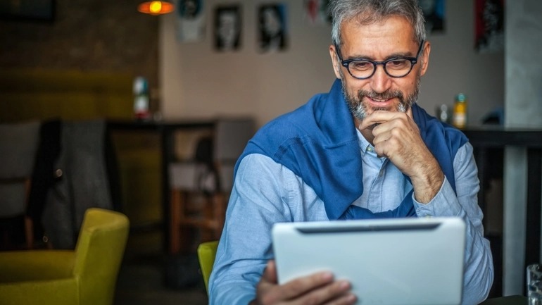 A man holds a tablet and reads while smiling