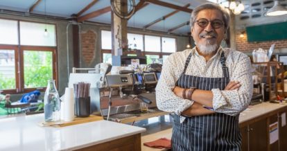 Smiling coffee shop owner standing in front of an espresso machine.