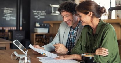 Smiling man and woman reviewing financial documents in a restaurant.