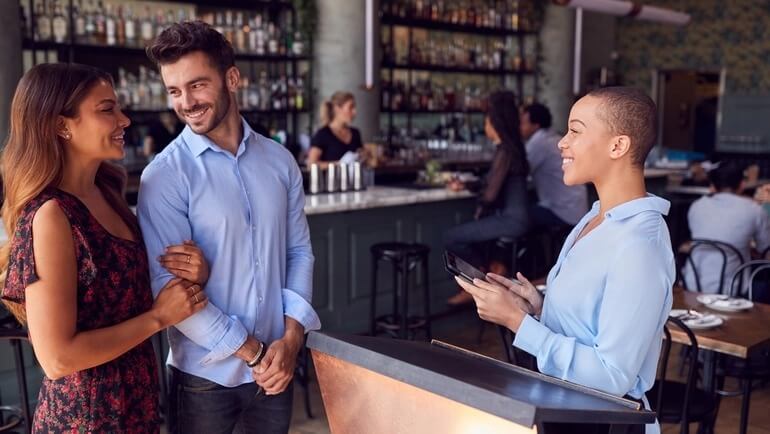 man and woman are greeted at a restaurant to check in