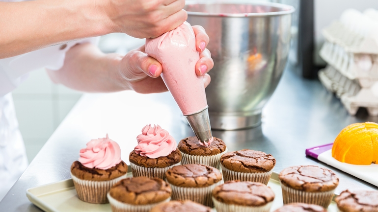 woman icing cupcakes with pink frosting in a bakery.