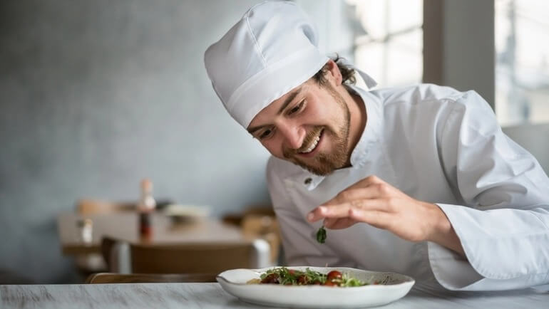 Male chef prepares a plate of food with greens and vegetables.