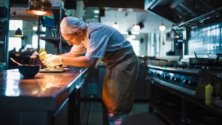 Male chef prepares a plate in restaurant with dressing.