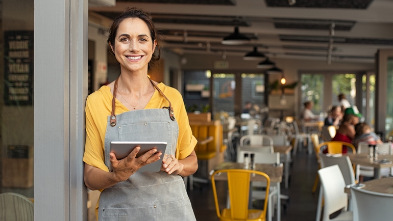 Female restaurant worker uses tablet and smiles.