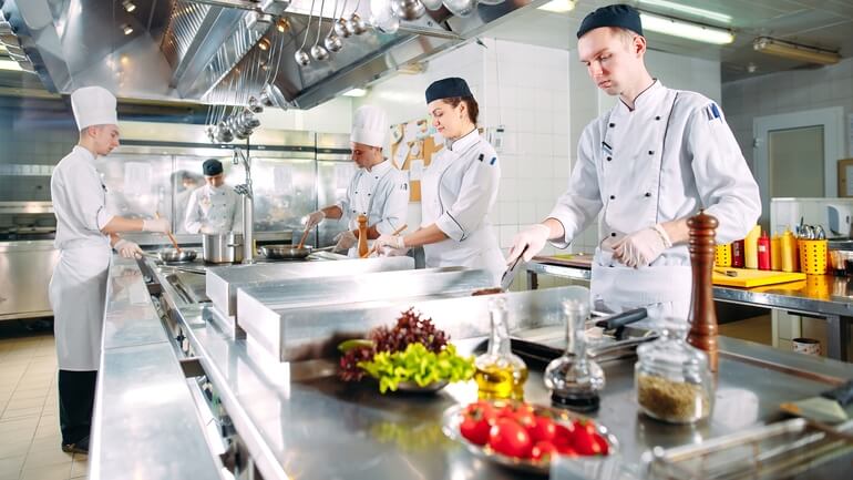 Restaurant chefs and workers prepare food in the back of a restaurant kitchen.