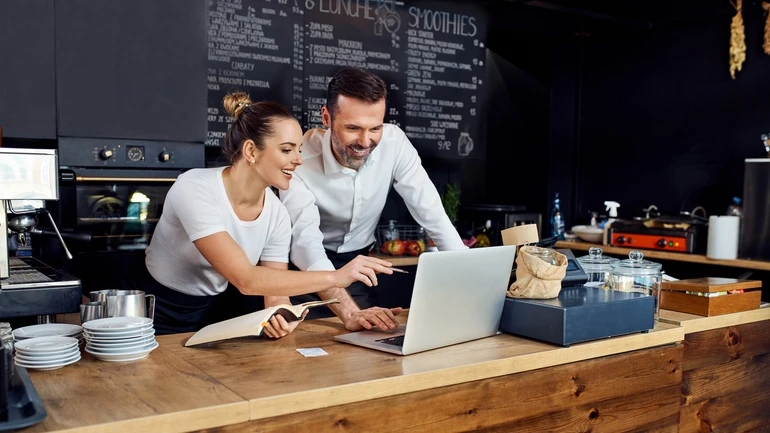 Two restaurant managers working on a laptop together and smiling.