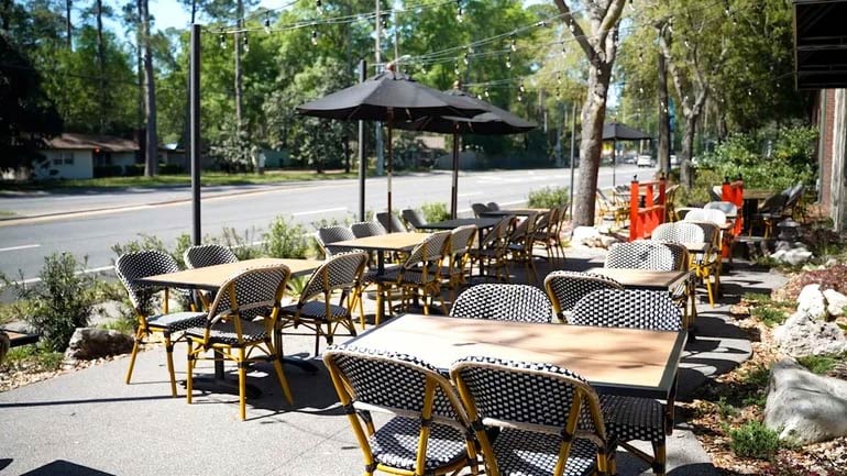 Empty restaurant patio with tables and chairs set up under patio umbrellas.
