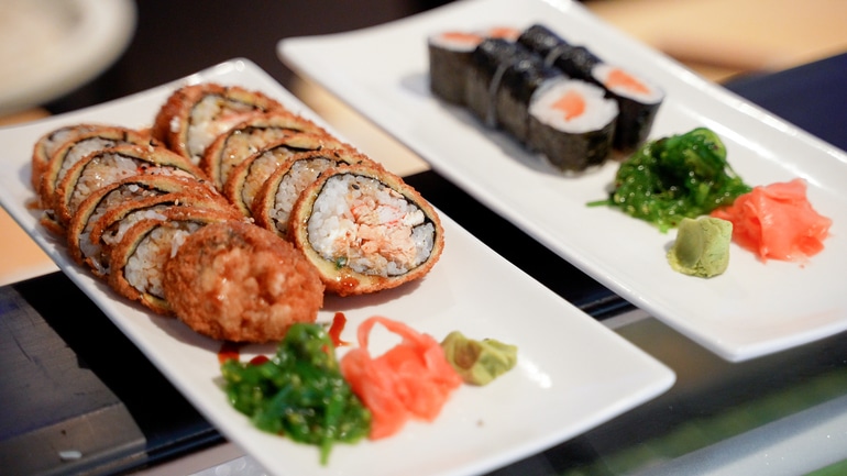 Two plates of sushi rolls with wasabi, ginger, and seaweed garnish.