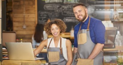 Male and Female restaurant worker smile at camera wearing aprons.