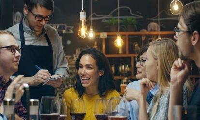 Group of friends enjoying a drink at a restaurant while a server takes their order.