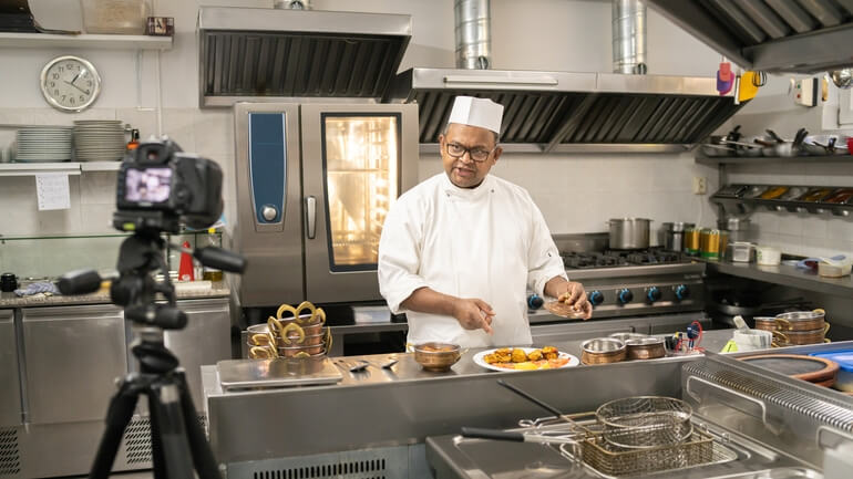 A chef films himself making food in a restaurant kitchen on camera.