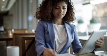 Woman taking notes and holding a tablet.