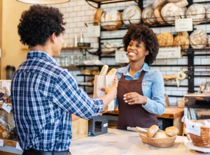 Image of a customer at a bakery picking up their order of bread from a bakery employee