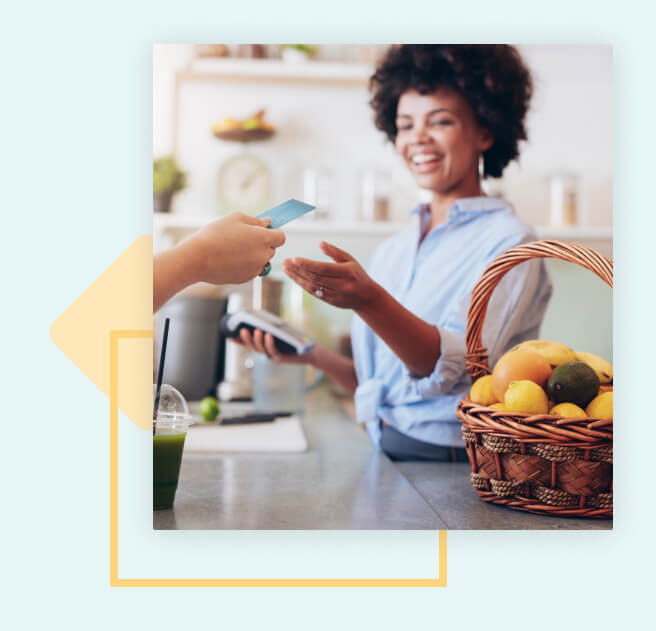 A customer handing their card to a female cashier, who has a payment terminal in their other hand.