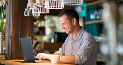 Portrait of a happy man working online at a cafe and drinking a cup of coffee