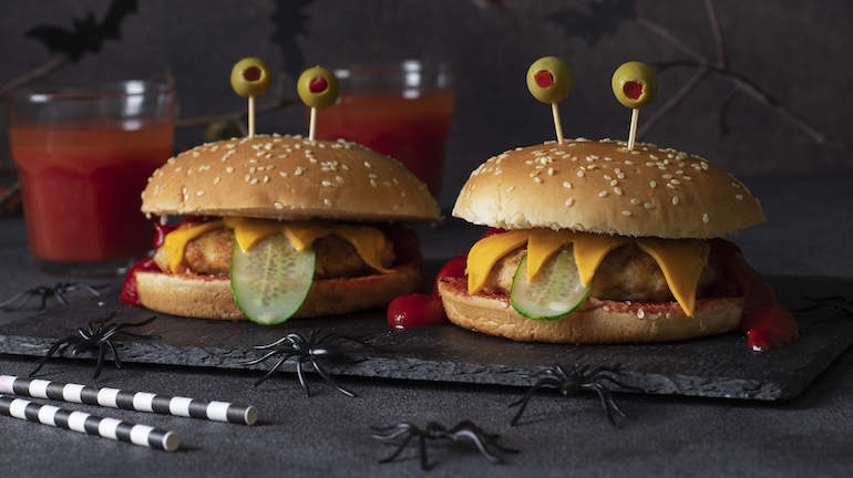 Two funny monster chicken burger with toast cheese, ketchup, green olives and cucumber. Creative Halloween food