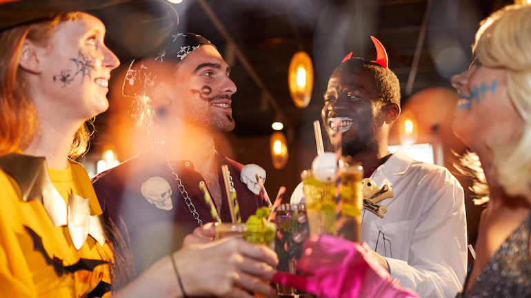 Multi-ethnic group of friends wearing Halloween costumes drinking cocktails while enjoying party in club and having fun