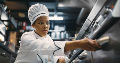 African American female chef preparing food in the oven while working at restaurant kitchen.
