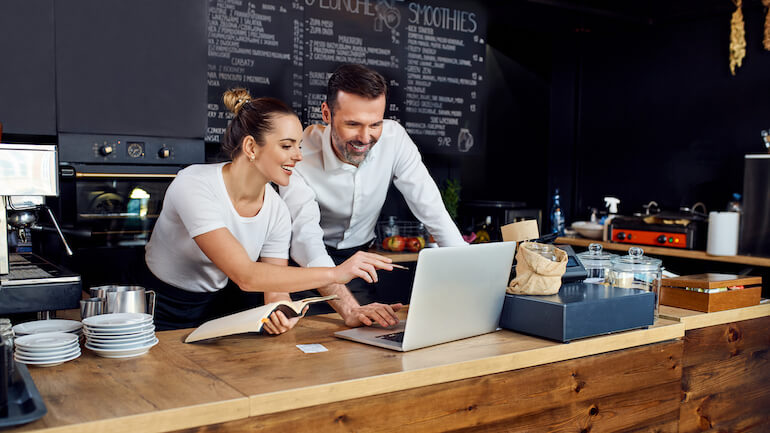 Male restaurant manager training female staff on laptop computer.