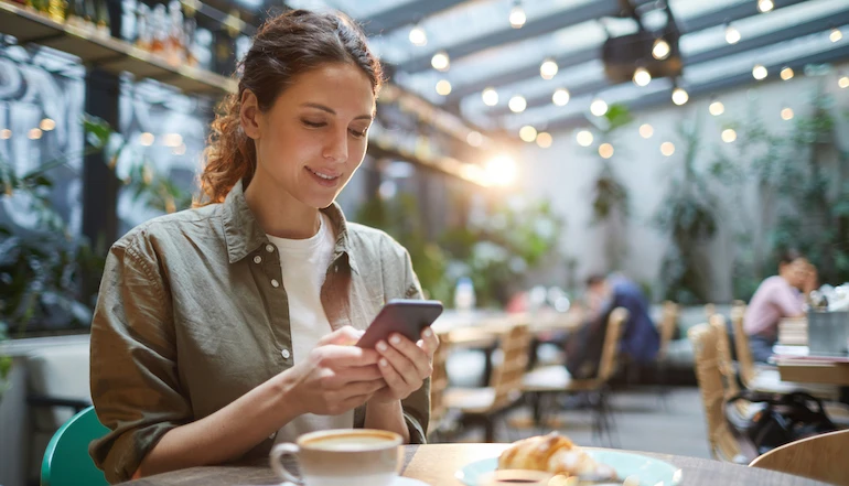 Portrait of beautiful young woman using smartphone while enjoying evening on outdoor terrace in cafe or coffee shop, copy space