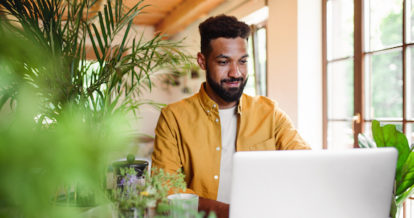 A young man with laptop and coffee working indoors, home office concept.