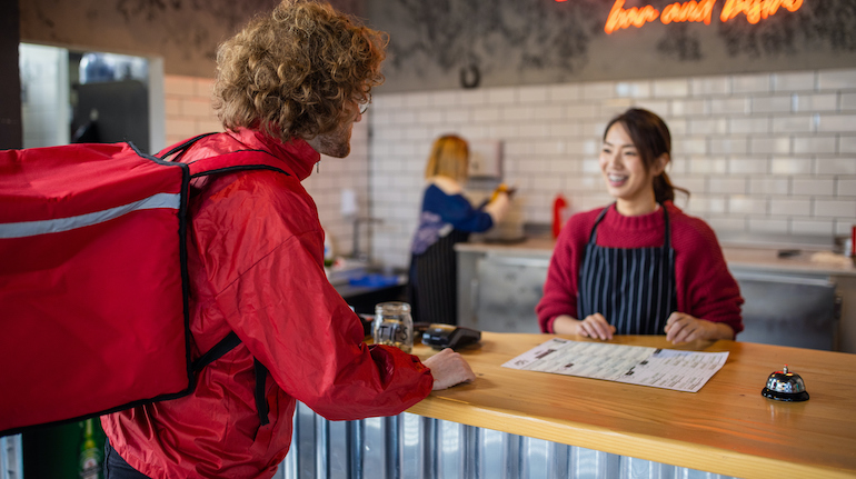 Male delivery person from DoorDash picks up an order from a modern fast food restaurant.