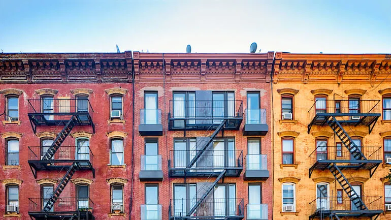 Top stories of colorful Williamsburg brownstone apartment buildings with steel fire escape stairways. Copy space in the sky above.