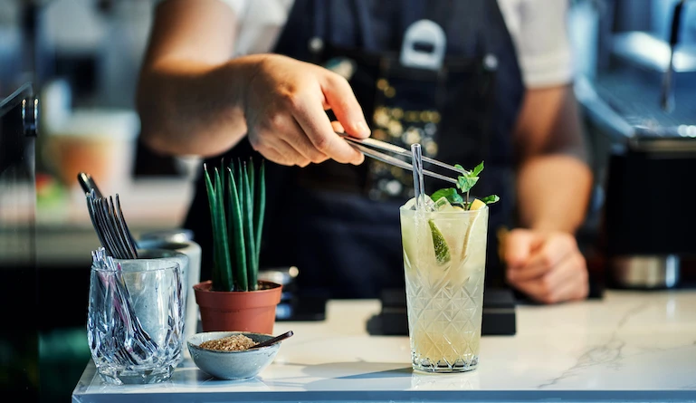 Close up of bartender mixing cocktail garnished with fresh mint leaves
