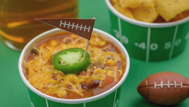 superbowl chili, beer, and party snacks closeup on green field background