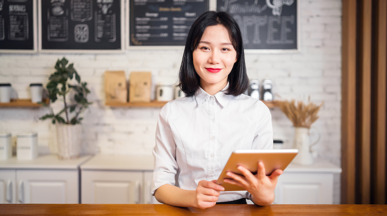 Confident female coffee shop owner holding an iPad tablet.