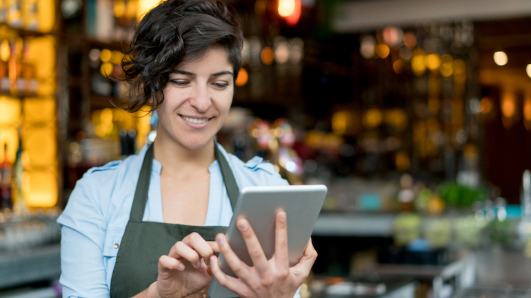 Happy waitress working at a restaurant and using app on a digital tablet