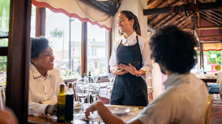 Smiling waitress taking order from a couple at a restaurant. Man and woman sitting at a restaurant and giving their lunch order to a female server.