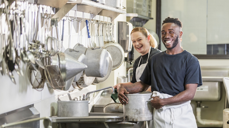 Two kitchen staff washing dishes in a commercial kitchen.