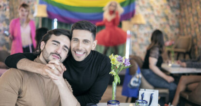 A male couple holding hands at a restaurant during a Pride Month celebration.